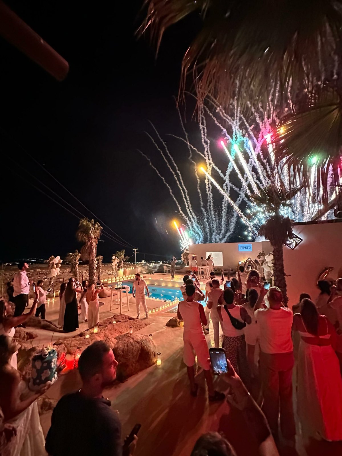 Guests watching fireworks over a villa pool party in Mykonos at night