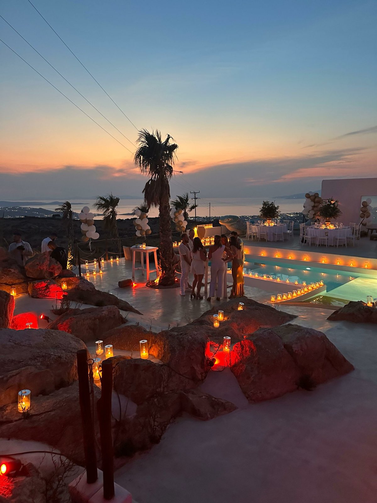 Sunset villa wedding in Mykonos. Candle-lit rocks, pool terrace and guests gathering as the light fades