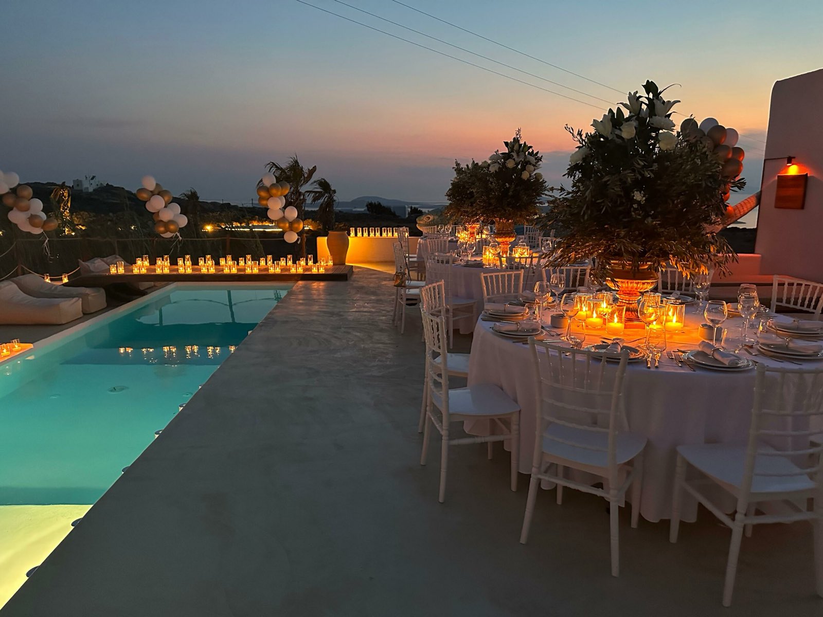 Wedding dinner tables beside a long villa pool in Mykonos at dusk with candles and warm lighting