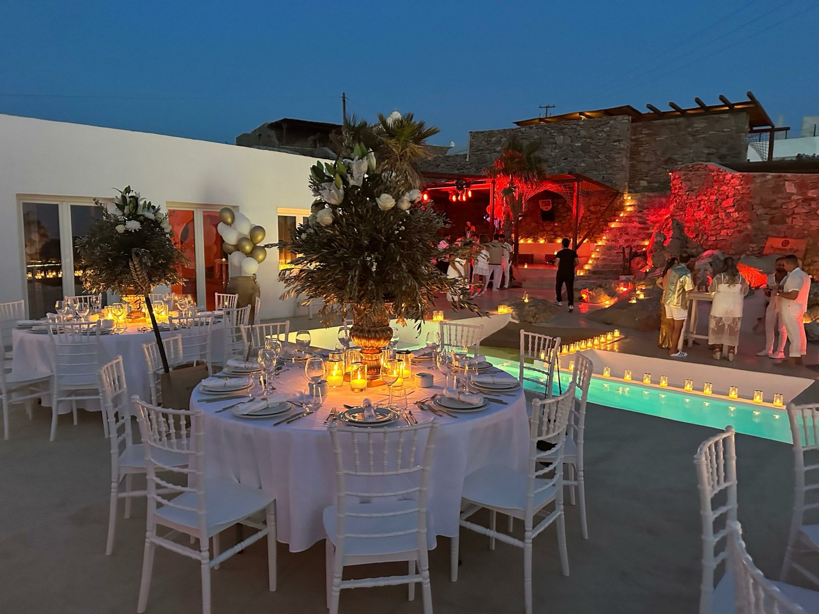 Wedding dinner tables on a Mykonos villa terrace lit with warm amber uplighting and candles